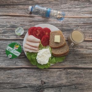 Zdjęcie przedstawia Dietę z ograniczeniem łatwoprzyswajalnych węglowodanów: Chleb Graham Masło extra Kawa zbożowa z mlekiem Serek twarogowy termizowany smak śmietankowy Kefir Pomidor Woda mineralna Szynkowa dębowa drobiowa kiełbasa grubo rozdrobniona Sałata zielona